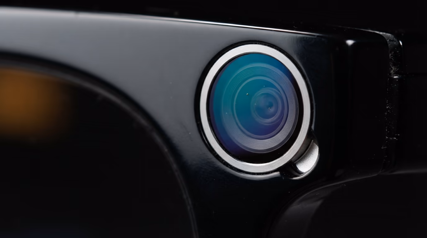Extreme macro of the camera lens set into the corner of a pair of black smart glasses