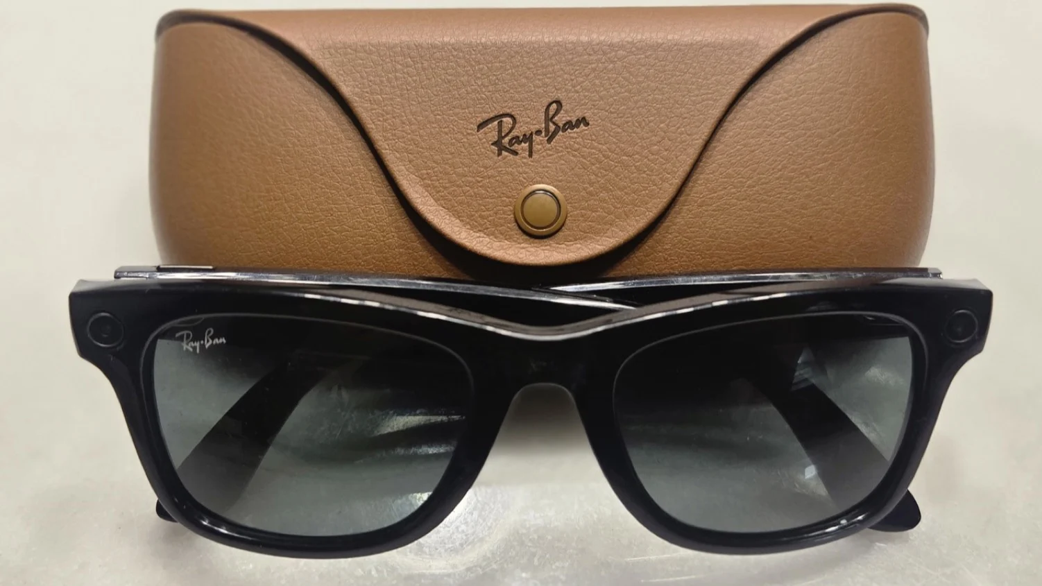 Ray Ban Meta smart glasses with a camera in the frame corner, lying in front of their case