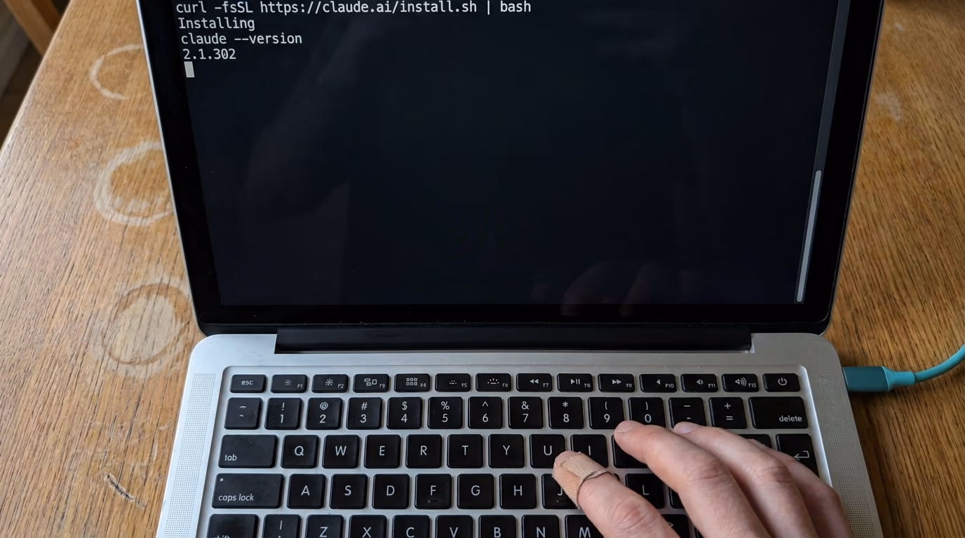 A laptop terminal showing the Claude Code install command and the version it prints afterwards