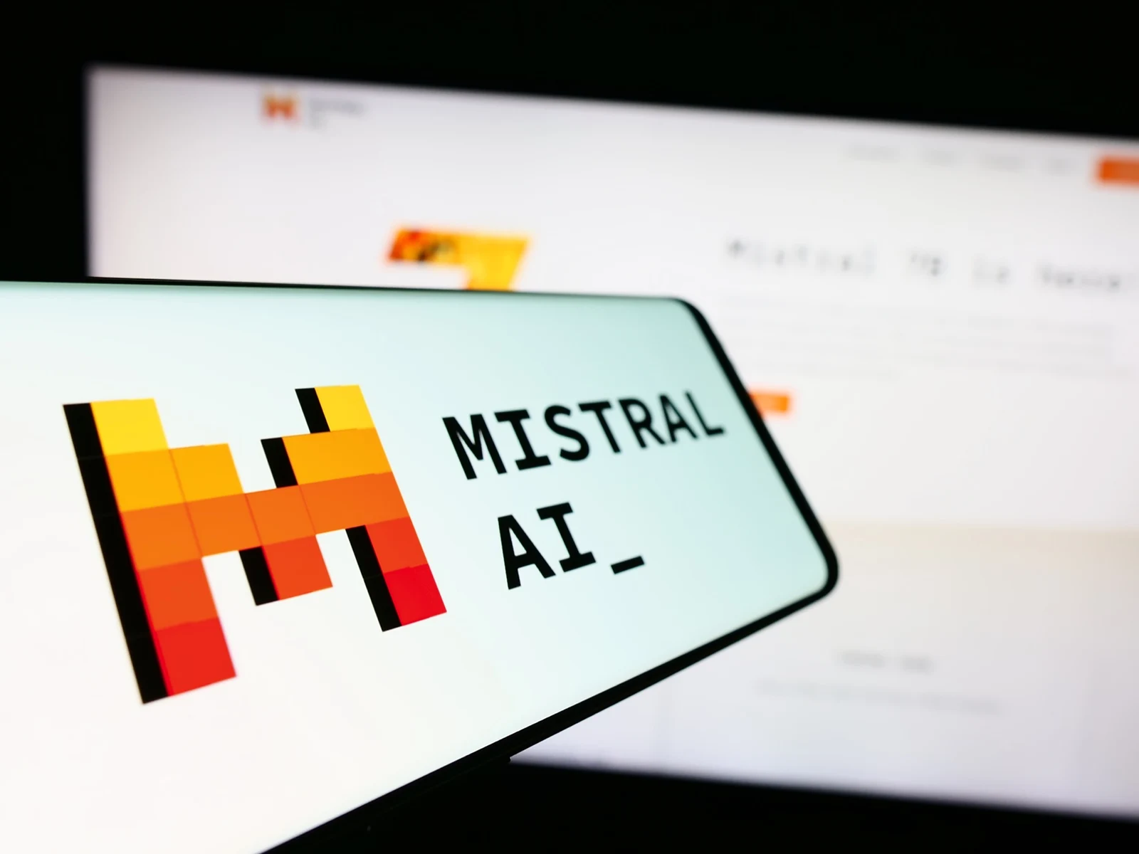 The Mistral AI logo on a phone screen held in front of the Mistral website